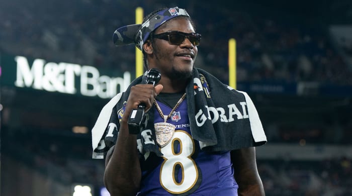 Lamar Jackson holds a mic on the sideline during a preseason game.